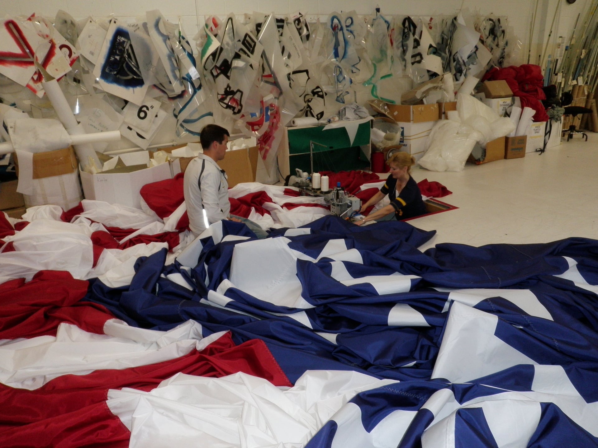 Two people sewing fabric in a workshop with flags nearby