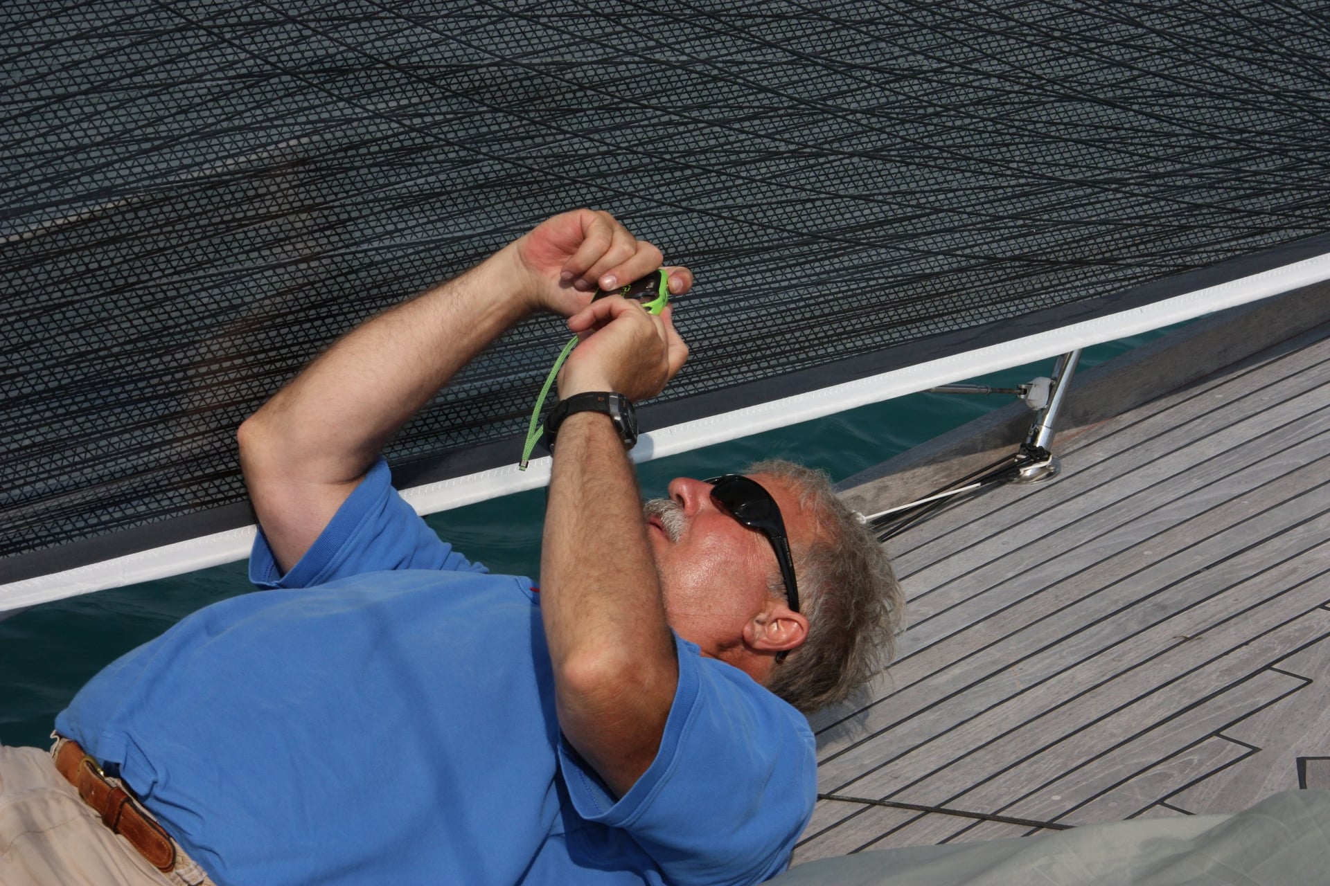 Man in a blue shirt lying on a sailboat deck, handling a line