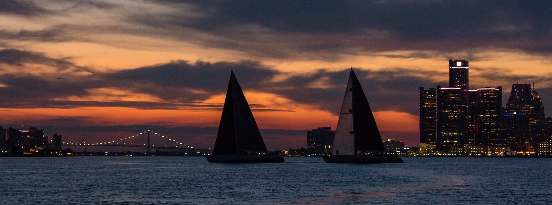 Two sailboats silhouetted at sunset with a city skyline