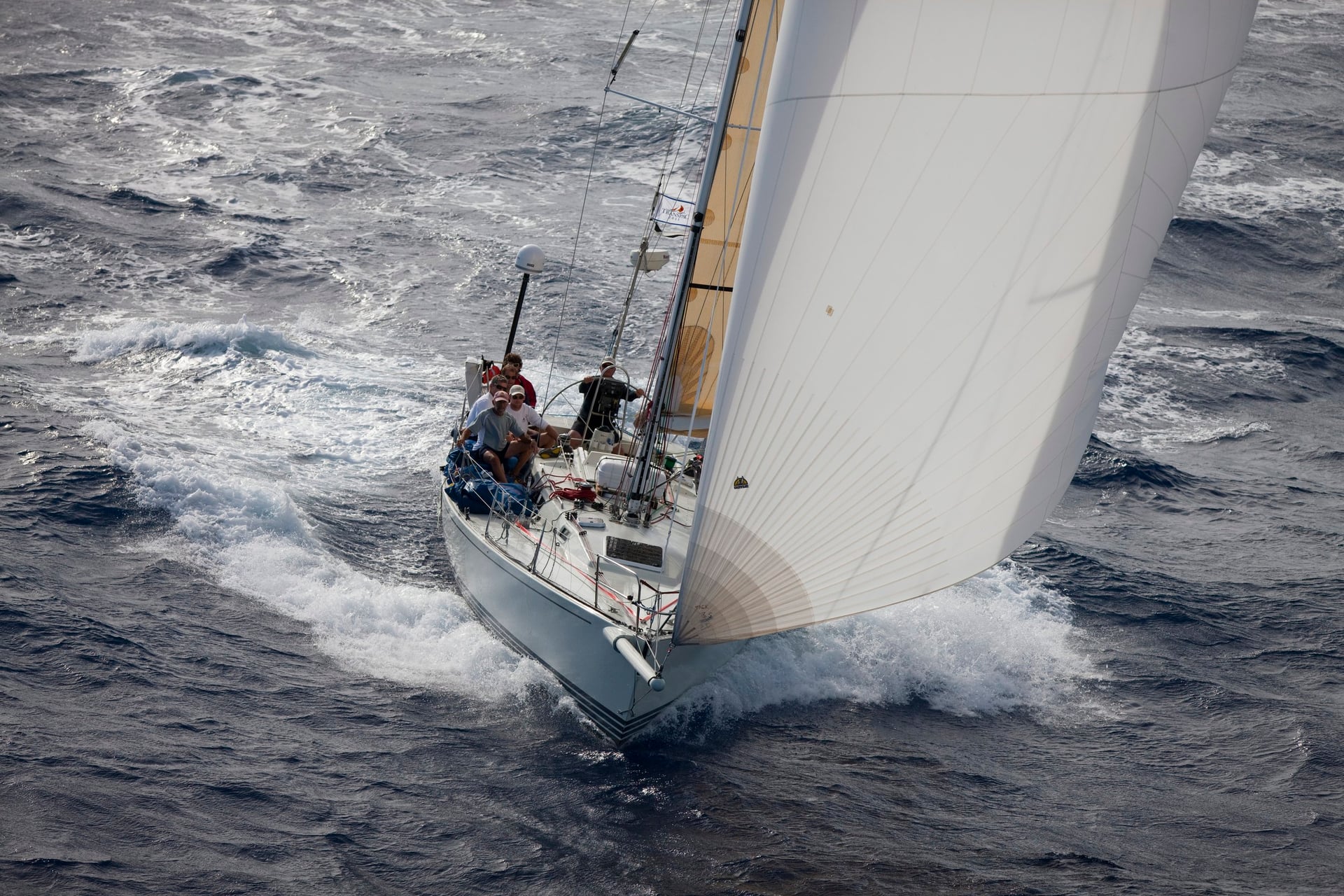Sailboat with a large white sail cutting through ocean waves
